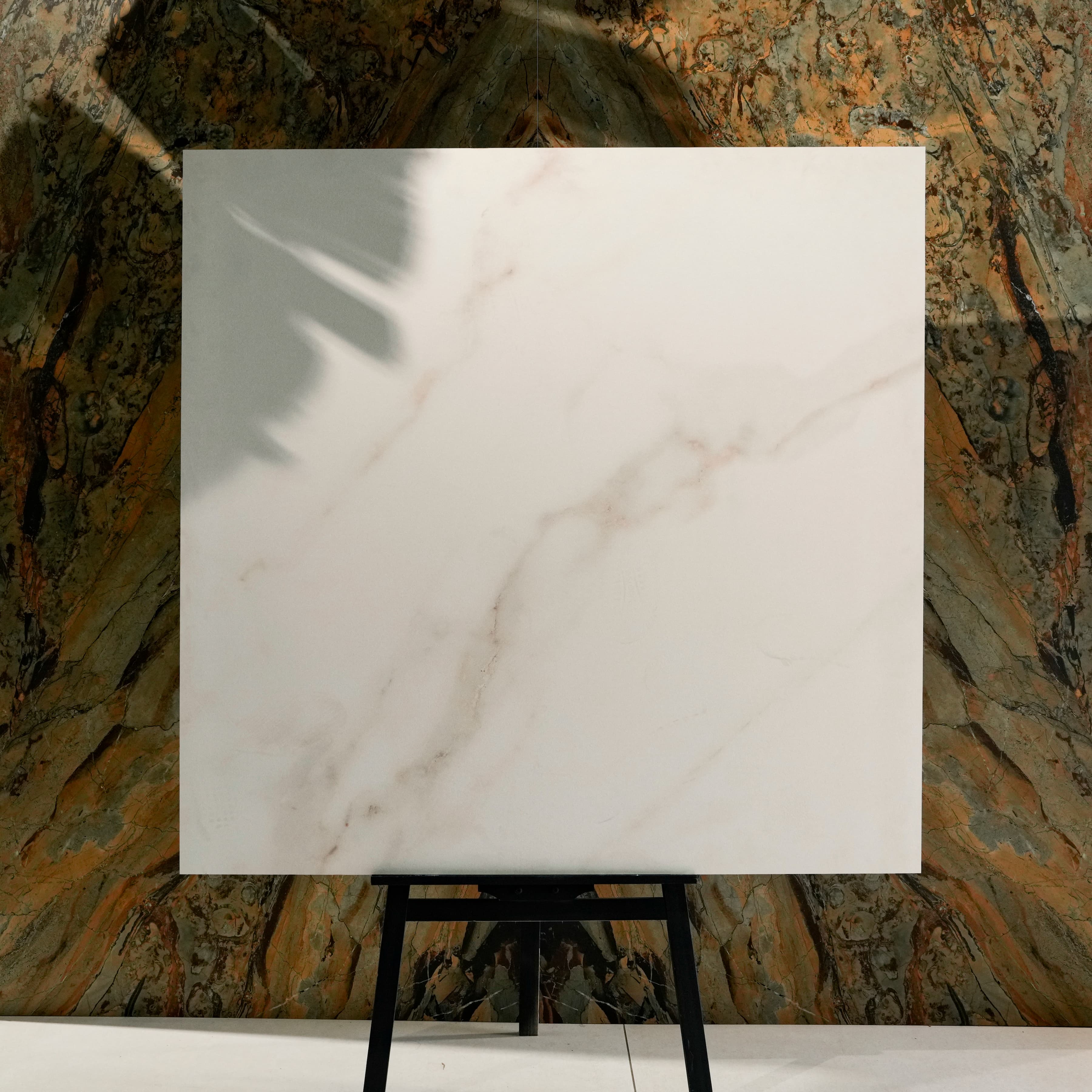 Cecelia Gold 120x120cm Calacatta gold marble effect matte porcelain tile on easel against onyx marble backdrop in UAE luxury tile showroom