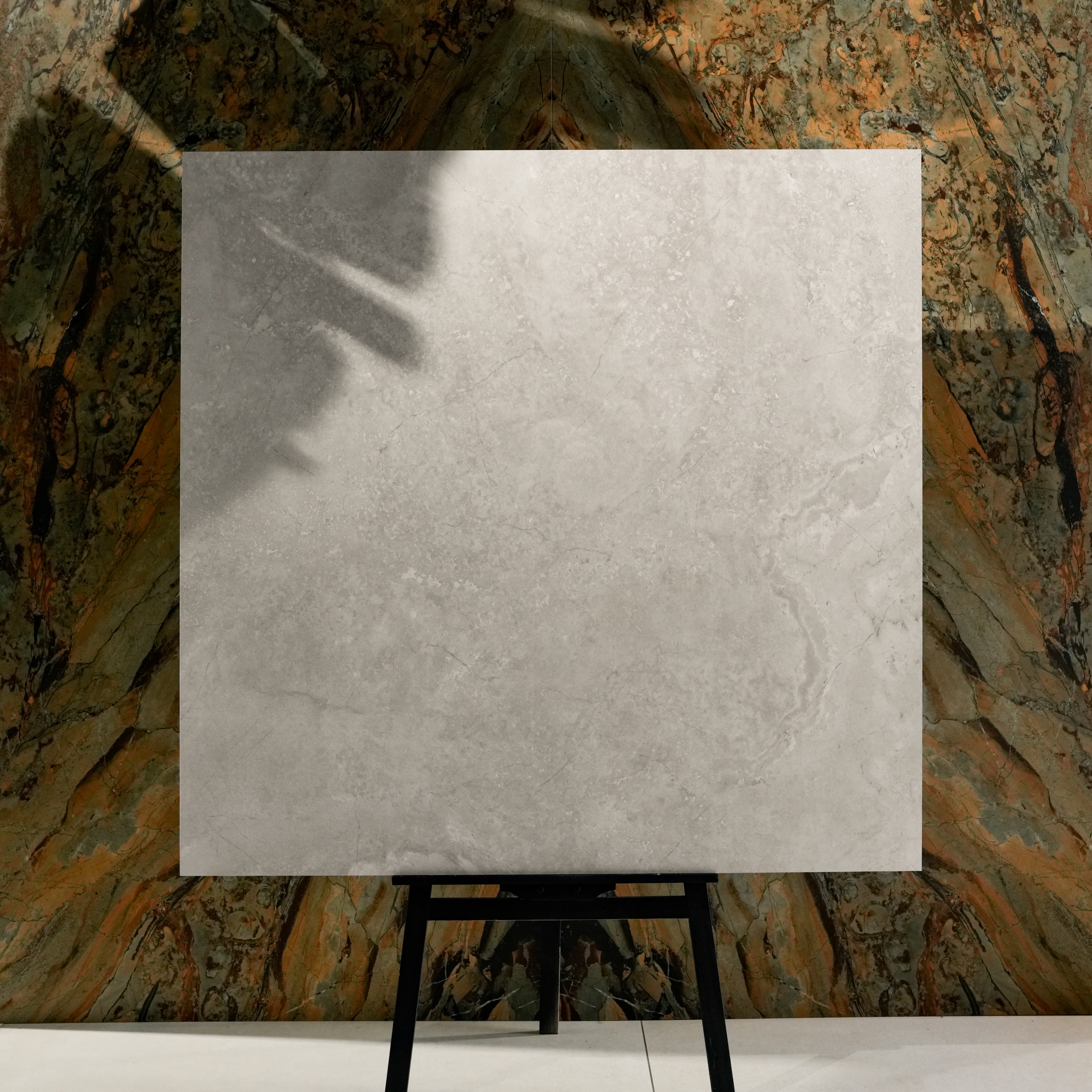 Resina Grey 120x120cm Italian resin effect weathered stone look matte porcelain tile on easel against onyx marble backdrop in UAE luxury tile showroom