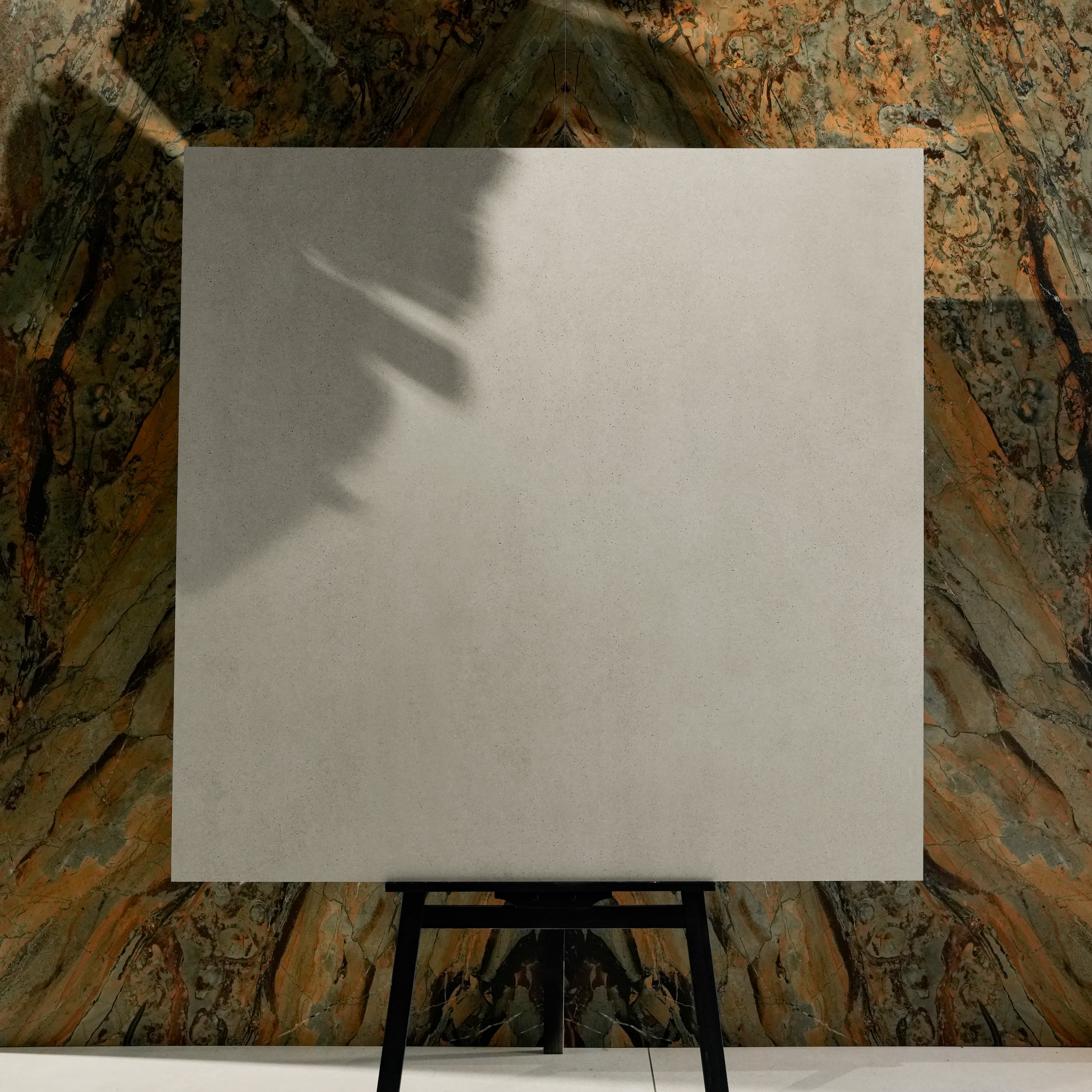 Vera Grey 120x120cm speckled stone-wash matte porcelain tile on easel against onyx marble backdrop in UAE luxury tile showroom
