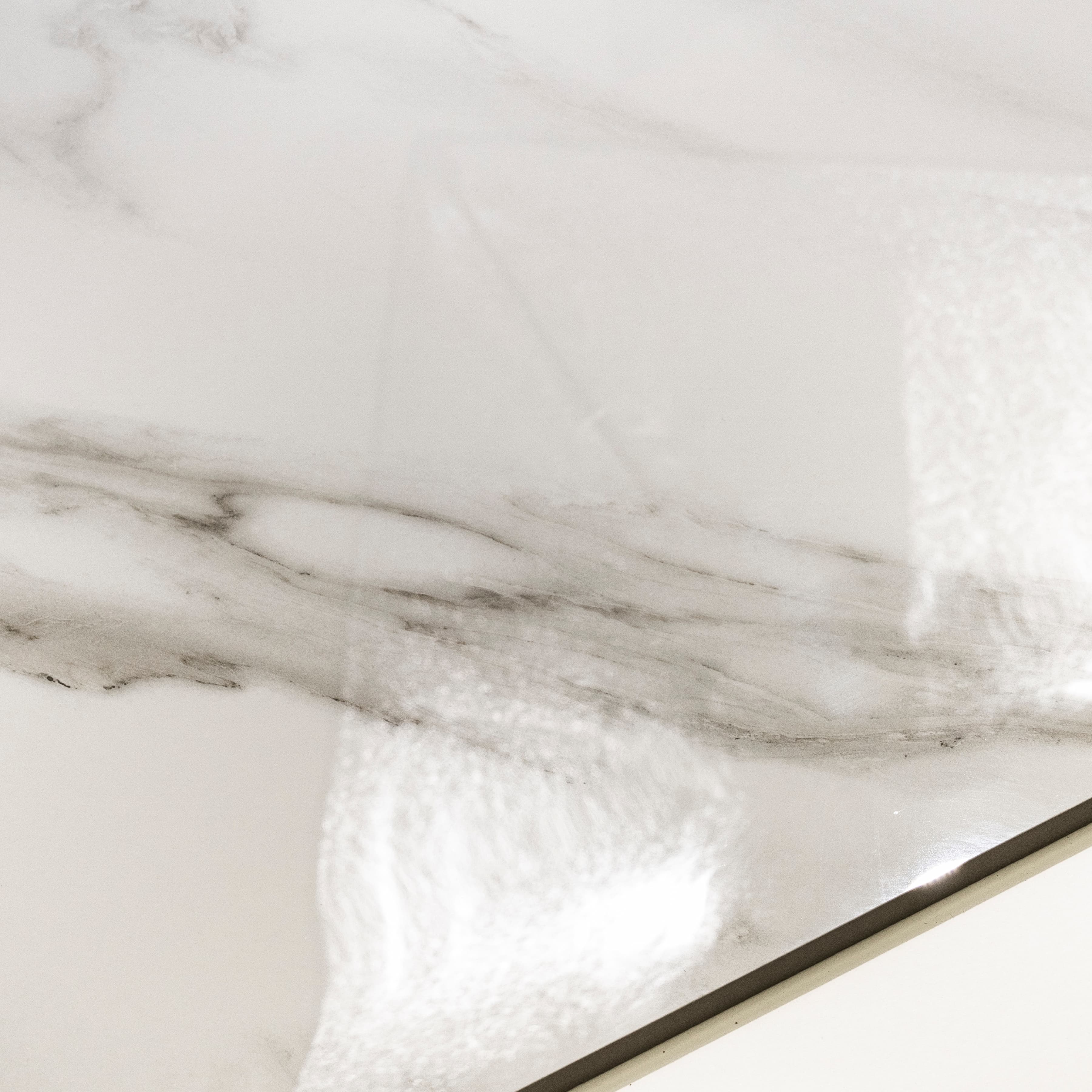 Close-up of Statuario Angel high-gloss polished porcelain surface revealing dramatic Statuario veining in soft warm grey and charcoal