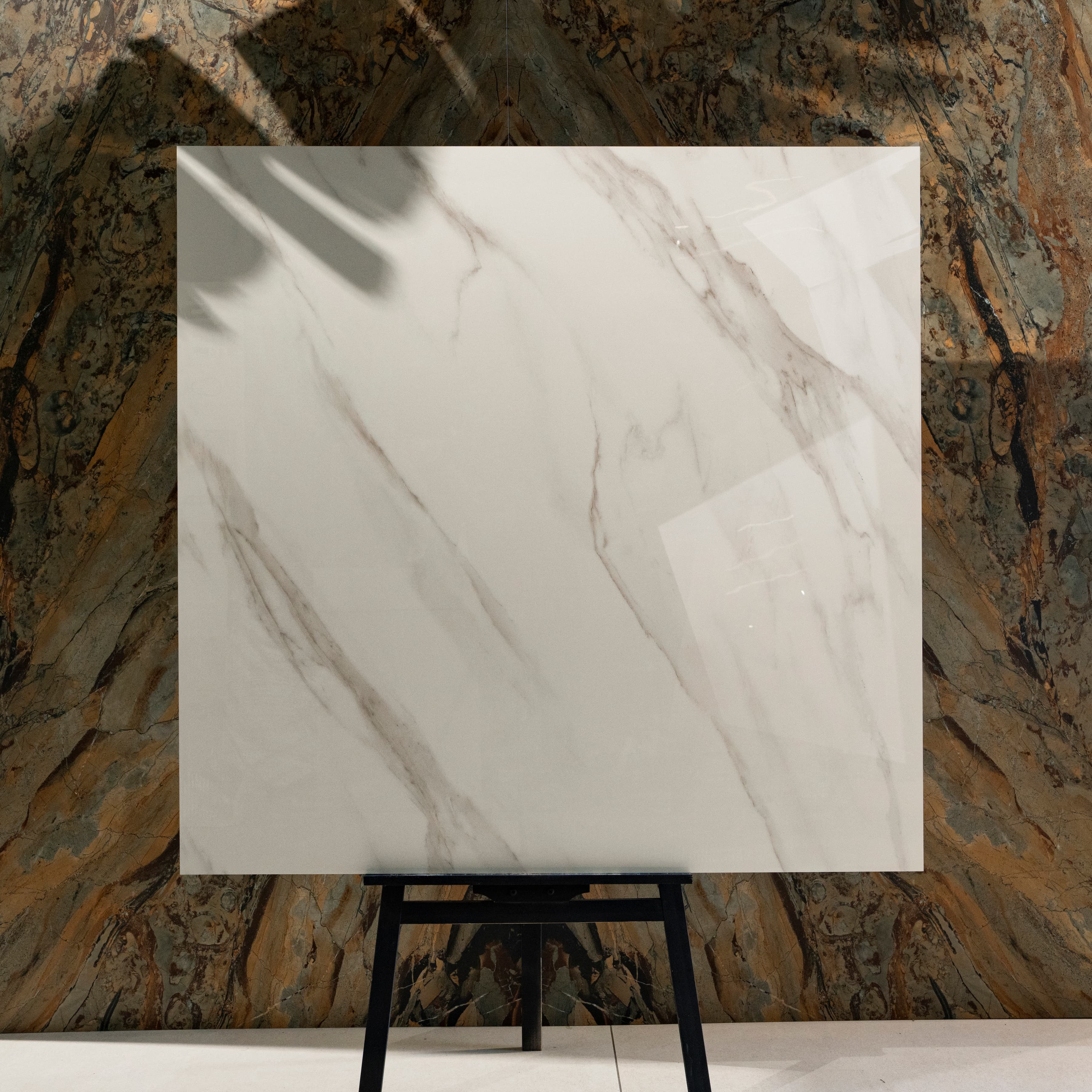 Statuario Angel 120x120cm glossy white Italian Statuario marble look polished porcelain tile on easel against onyx marble backdrop in UAE luxury tile showroom