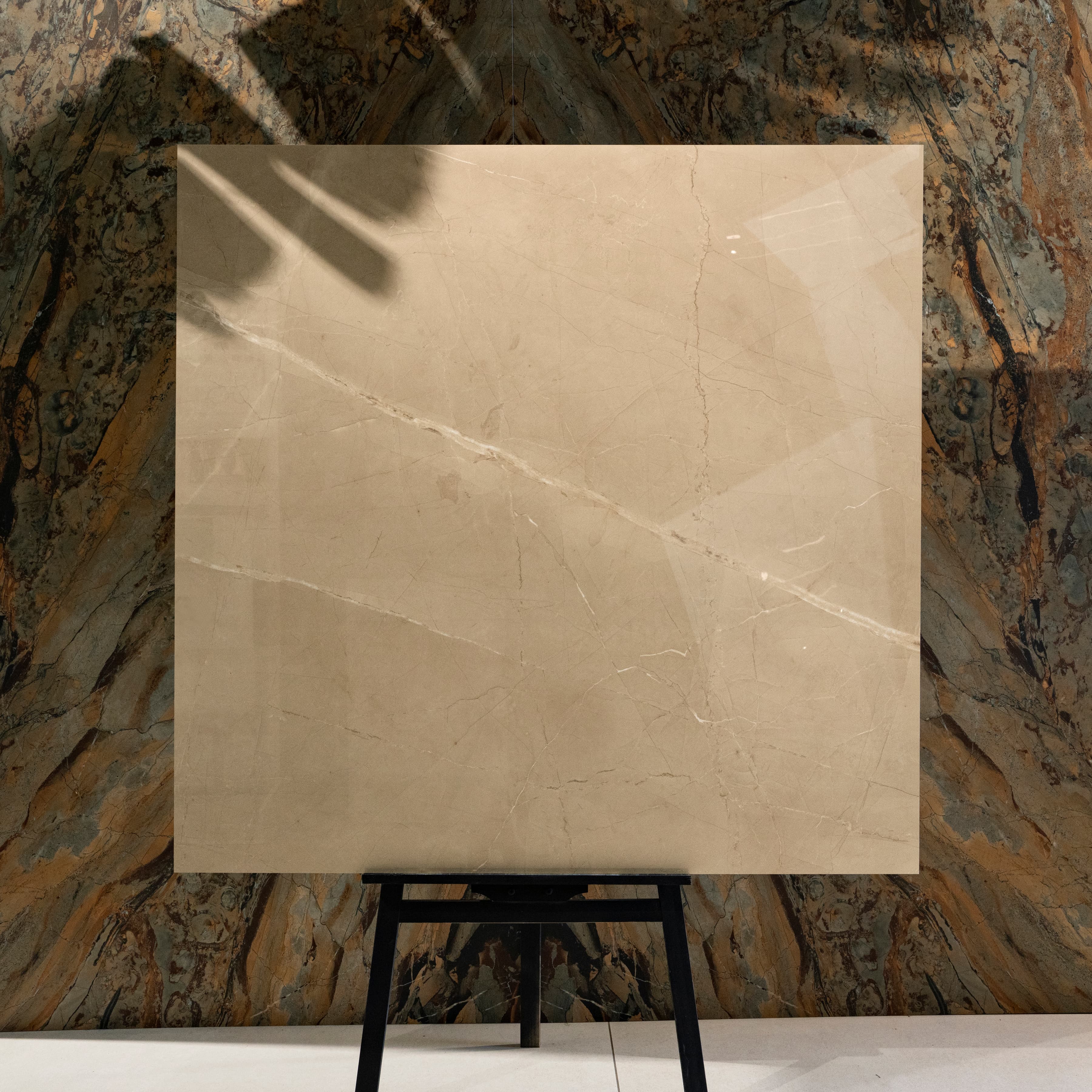 Armani Beige 120x120cm warm Italian Crema Marfil look glossy polished porcelain tile on easel against onyx marble backdrop in UAE luxury tile showroom